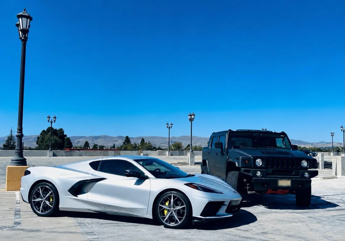 Chevrolet Corvette C8 blanco de perfil, estacionado junto al Hummer H2